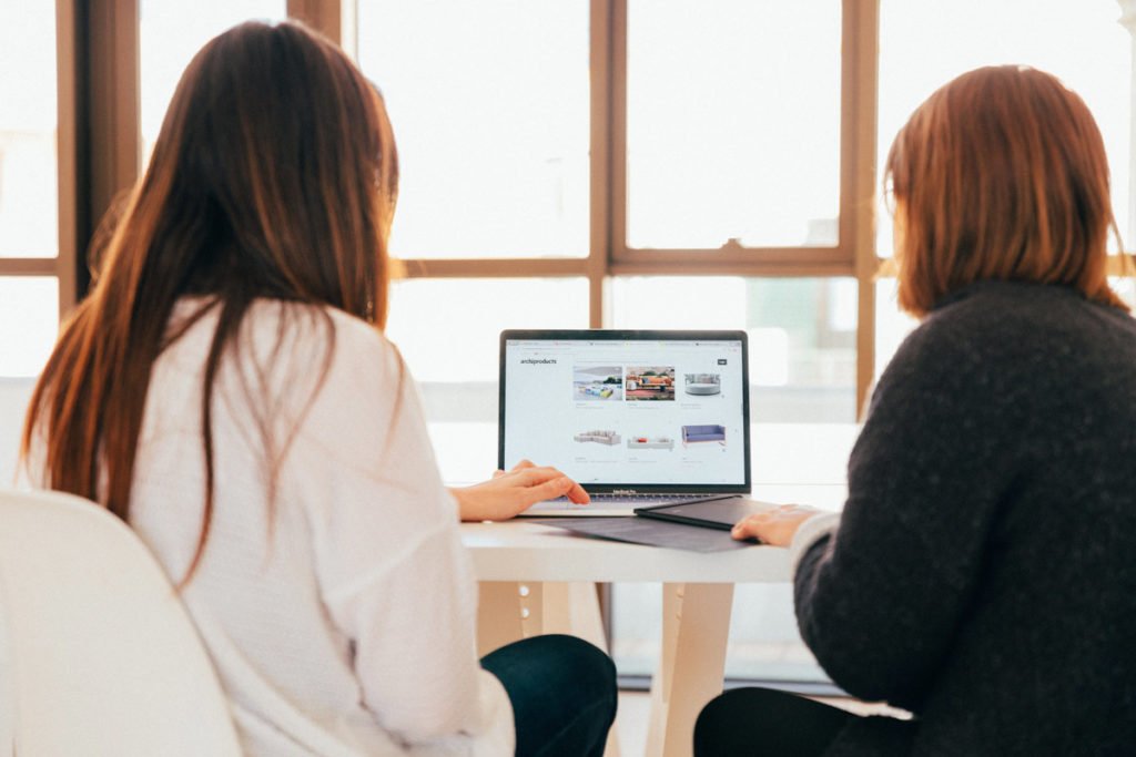 Two woman sitting at desk as they go through furniture store online